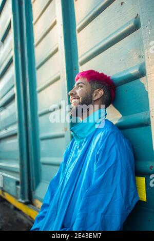Young man with stylish pink-dyed hair wearing a retro jacket leaning against a railway wagon Stock Photo