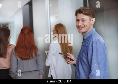 Cheerful male entrepreneur smiling to the camera, using smart phone at workplace Stock Photo