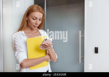Attractive female entrepreneur using her smart phone, walking at office building Stock Photo