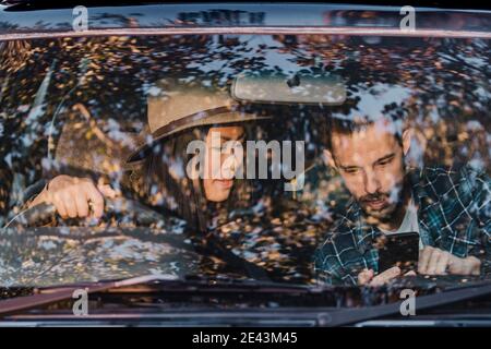 Multiethnic couple of travelers sitting in car and searching for route while using GPS map on mobile phone during trip in Australia Stock Photo