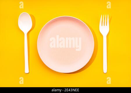 Top view composition with white plastic spoon and fork arranged near empty plate on yellow background Stock Photo