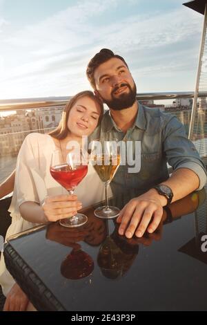 Vertical shot of two young people in love cuddling on sunset, drinking wine at bar terrace Stock Photo