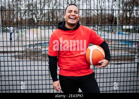 Portrait of a latino man posing by the fence of a basketball court. Looking at camera as he smiles. Stock Photo