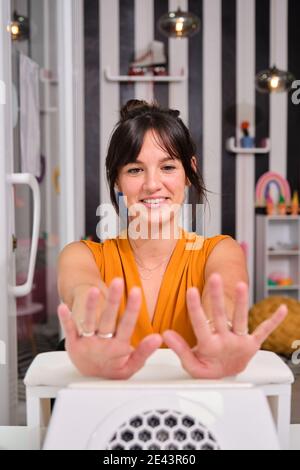 Delighted young female client looking at fingers and smiling being happy with perfect manicure after treatment in beauty salon Stock Photo