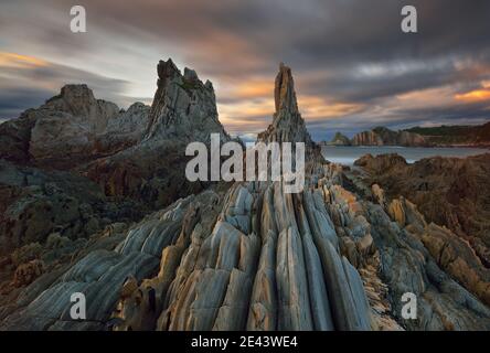 Long exposure sunset on the row of sharp stone islets emerging from the ocean, remains of an ancient fractured point of quartz and slate. This area is Stock Photo