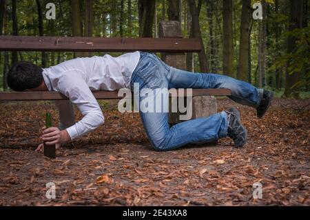 Depressed drunk man asleep outdoor on a park bench with beer bottles Stock Photo