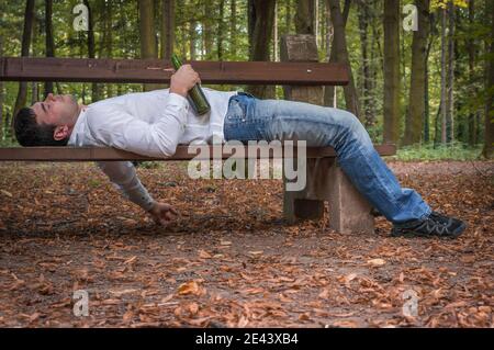 Depressed drunk man asleep outdoor on a park bench with beer bottles Stock Photo