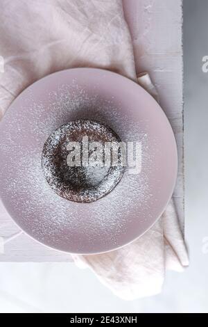 Top view of delicious chocolate fondant sprinkled with sugar powder served on plate on napkin on pink background Stock Photo