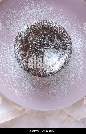 Top view of delicious chocolate fondant sprinkled with sugar powder served on plate on napkin on pink background Stock Photo