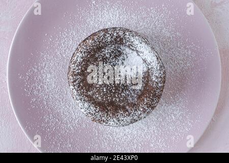 Top view of delicious chocolate fondant sprinkled with sugar powder served on plate on napkin on pink background Stock Photo
