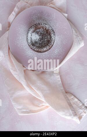 Top view of delicious chocolate fondant sprinkled with sugar powder served on plate on napkin on pink background Stock Photo