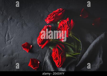 Top view composition of bright red blooming rose buds and petals scattered on black surface with cloth Stock Photo