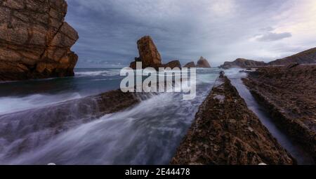 Dramatic landscape of foamy waves washing rough rocky formations under stormy cloudy sky on Playa de la Arnia or Arnia Beach in Cantabria in Spain Stock Photo