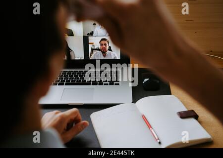 Back view of smiling male manager having video conference online via laptop while sitting at table and working from home during coronavirus epidemic Stock Photo