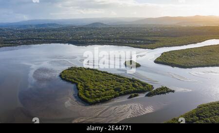 Picturesque drone view of heart shaped island covered with lush green vegetation washing by river water against sunset sky in countryside in Australia Stock Photo