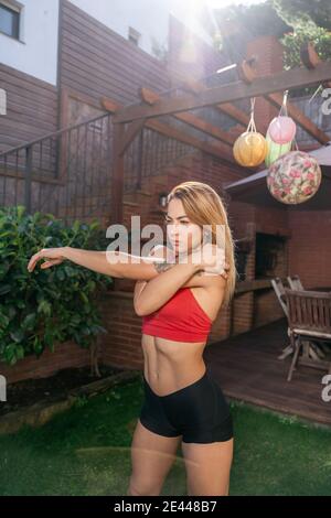 Focused female athlete doing stretching body while warming up before workout in backyard Stock Photo
