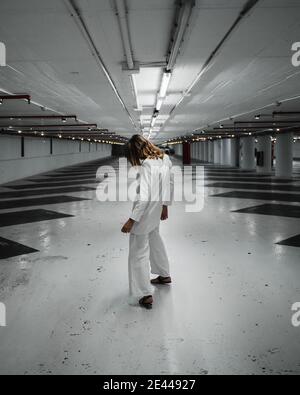 Side view of anonymous lady in stylish total white outfit standing in empty underground parking lot Stock Photo