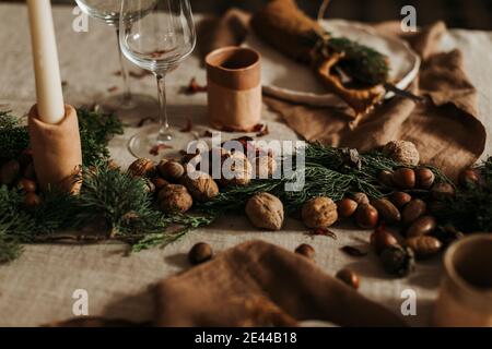 Various nuts scattered near green fir branches and candles on festive table decorated in rustic style for Christmas celebration Stock Photo