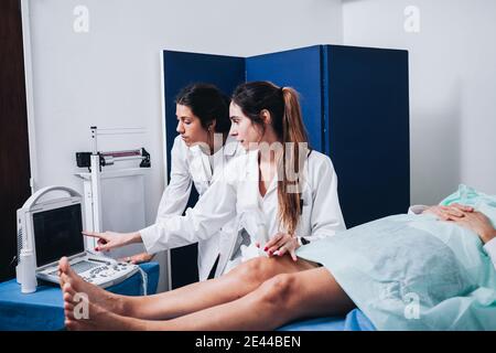 Two female doctors are making an ultrasound to the legs of a patient that is lying on a stretcher in an hospital Stock Photo