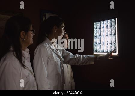 A group of female doctors are looking a x-ray in a dark room with the light off and one is pointing it Stock Photo