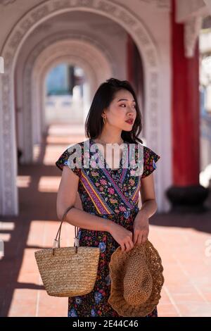 Delighted Asian female traveler standing in arched passage of Cikang Overpass bridge and looking away while enjoying sightseeing during summer vacatio Stock Photo