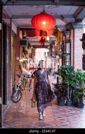 Young Asian female in long dress walking along historic Daxi Old Street and looking away while enjoying vacation in Taiwan Stock Photo