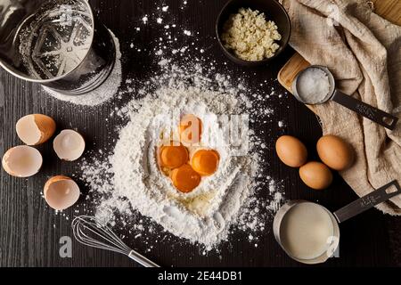 Top view of yolks in flour on wooden table with utensils and ingredients prepared for cooking cake Stock Photo