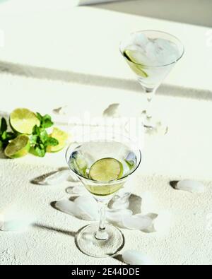 High angle of cold mojito cocktail in glasses with lime slices and ice cubes placed on white table with mint sprigs Stock Photo