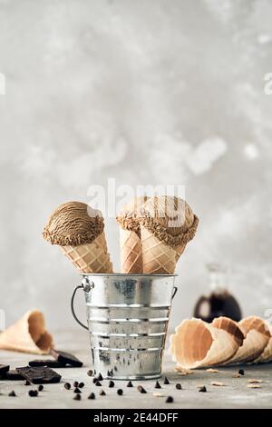 Scoops of chocolate ice cream in waffle cones in metal bucket placed on table Stock Photo