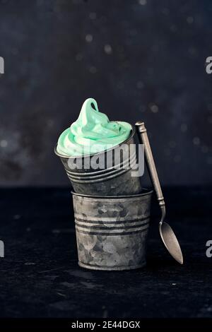 Sweet green mint ice cream in metal bucket placed on table with spoon on dark background in studio Stock Photo