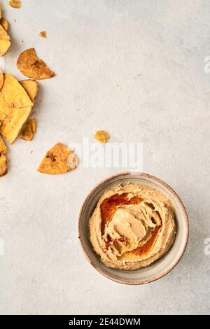 Top view of hummus bowl and crispy potato chips placed on gray background Stock Photo