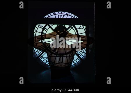 Back view of unrecognizable black female with hands behind head standing under shade of clock in dark room Stock Photo