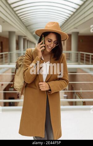 Smiling female student in smart casual outfit standing in university hallway and messaging on mobile phone Stock Photo
