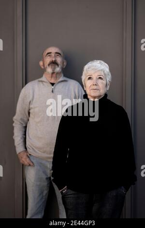 Front view of an older couple by a gray wall in black and gray clothes Stock Photo