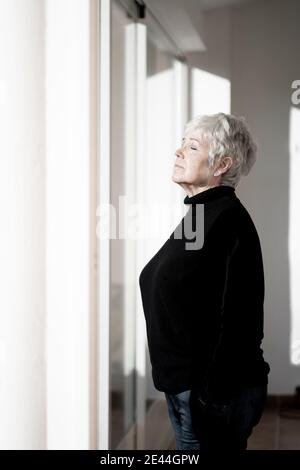 Relaxed senior Woman at home by the window on a sunny day Stock Photo