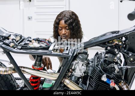 African American female mechanic with wrench fixing custom motorbike while working in workshop Stock Photo