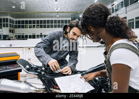 Side view of multiracial male and female mechanics repairing custom motorbike in spacious workshop while working together Stock Photo