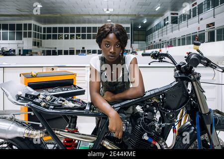 Professional young African American female mechanic looking at camera while assembling custom motorbike in modern workshop Stock Photo