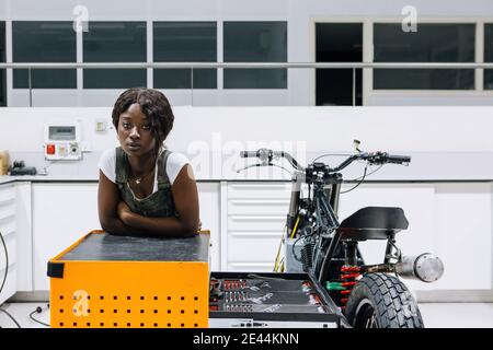 Professional young African American female mechanic looking at camera while assembling custom motorbike in modern workshop Stock Photo