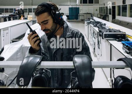 Professional male master in workwear and headset using walkie talkie for communication while working in modern mechanical workshop Stock Photo