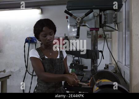 Skilled African American female master in overall handling detail on lathe machine while working in professional workshop Stock Photo