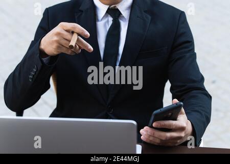 Confident Asian male entrepreneur sitting at table in cafe and smoking cigar while browsing smartphone Stock Photo