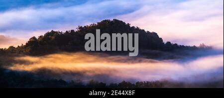 Spectacular landscape of fluffy clouds floating over mountains covered with lush trees in sunny morning Stock Photo