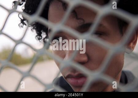 Side view of thoughtful teen African American male with curly hair looking away while standing behind metal chain link fence on urban street Stock Photo