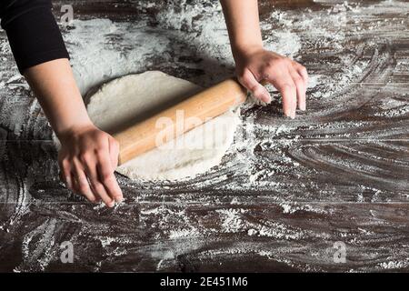 From above of crop anonymous female baker rolling dough on table sprinkled with flour while preparing bread in bakery kitchen Stock Photo