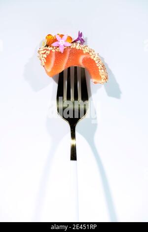 Piece of tasty salmon sashimi decorated with caviar and herbs on fork against white background Stock Photo