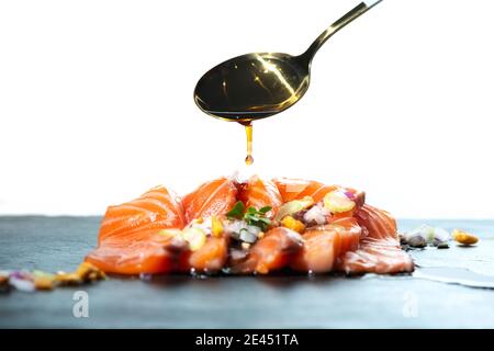 Unrecognizable person adding spoon of soy sauce on delicious salmon fillet dish garnished with herbs against white background Stock Photo