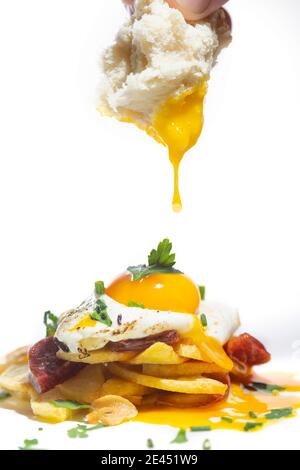 Crop unrecognizable person with piece of bread in hand eating delicious dish with potatoes and beets garnished with fried egg against white background Stock Photo