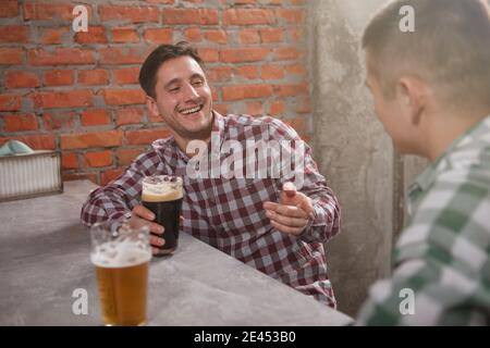 Cheerful man laughing, talking to his friend over glass of beer Stock Photo