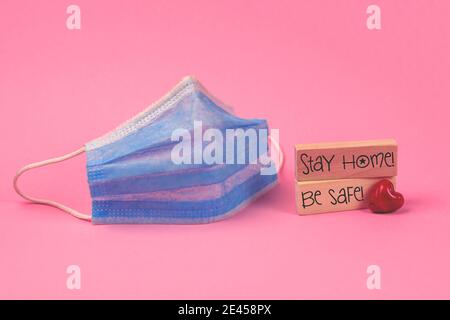 Stay home concept with a medical mask on a pink bakground, with wooden blocks, tetxt inscription and red heart, valentine's day holiday photo Stock Photo